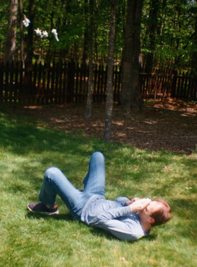 Bard Photographing Bones In The Sky laying on the grass with bones floating above him